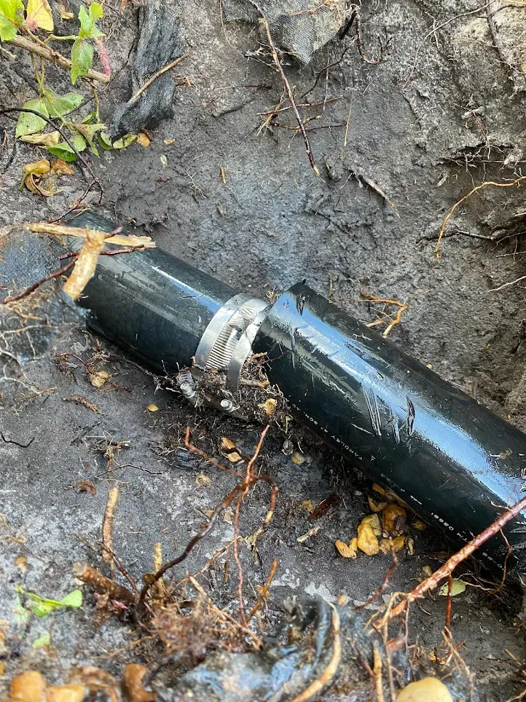 A black pipe is laying on the ground in the dirt.