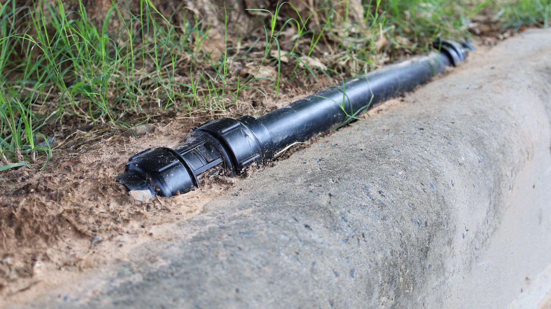 A black pipe is laying on the side of a road.