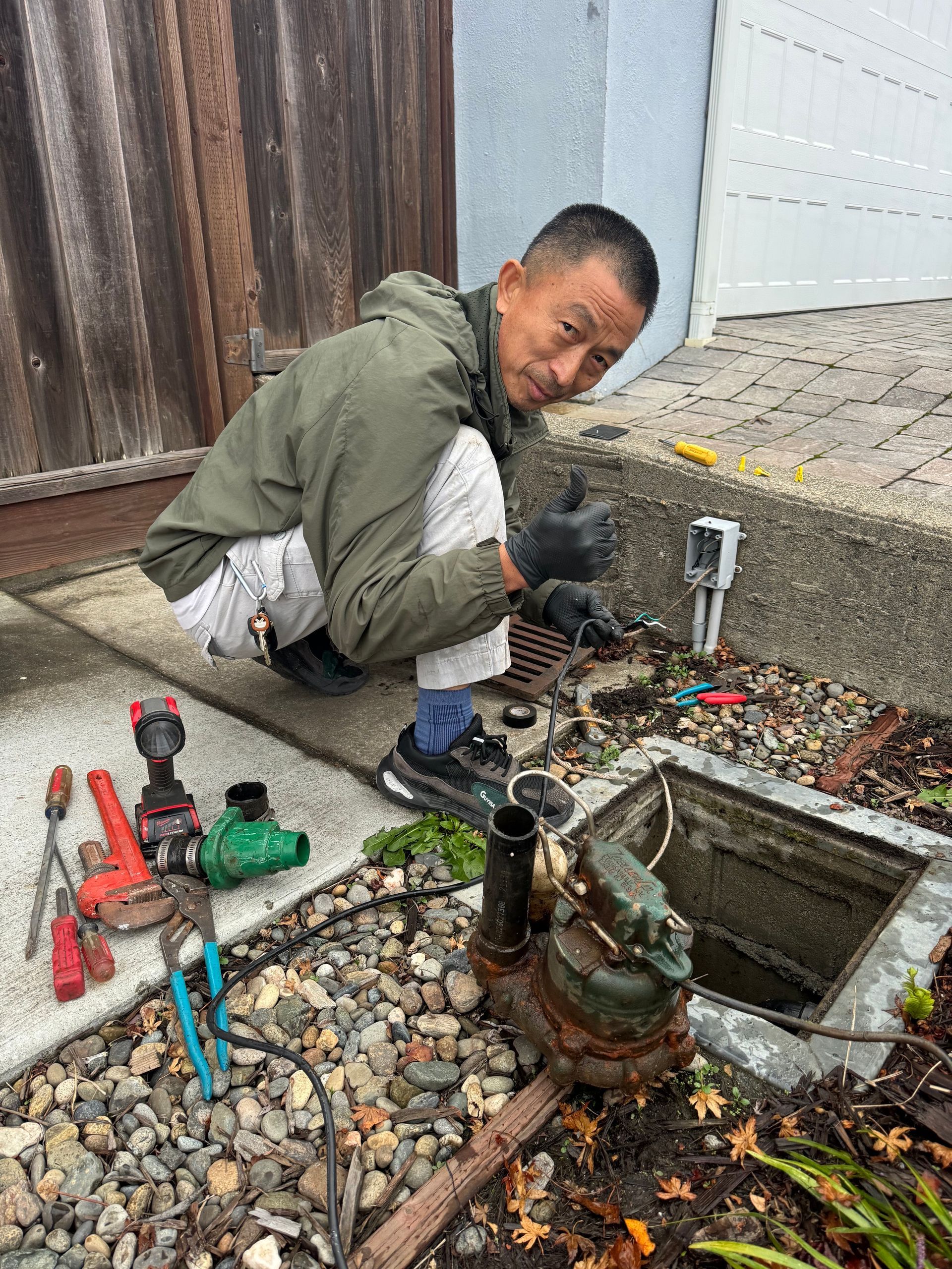 A man is kneeling on the ground working on a pipe.