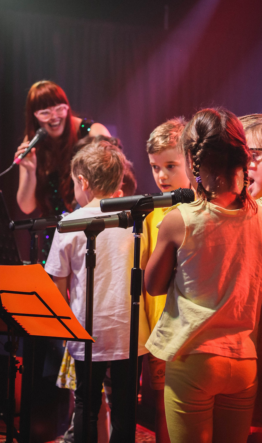 A group of children are singing into microphones on a stage.