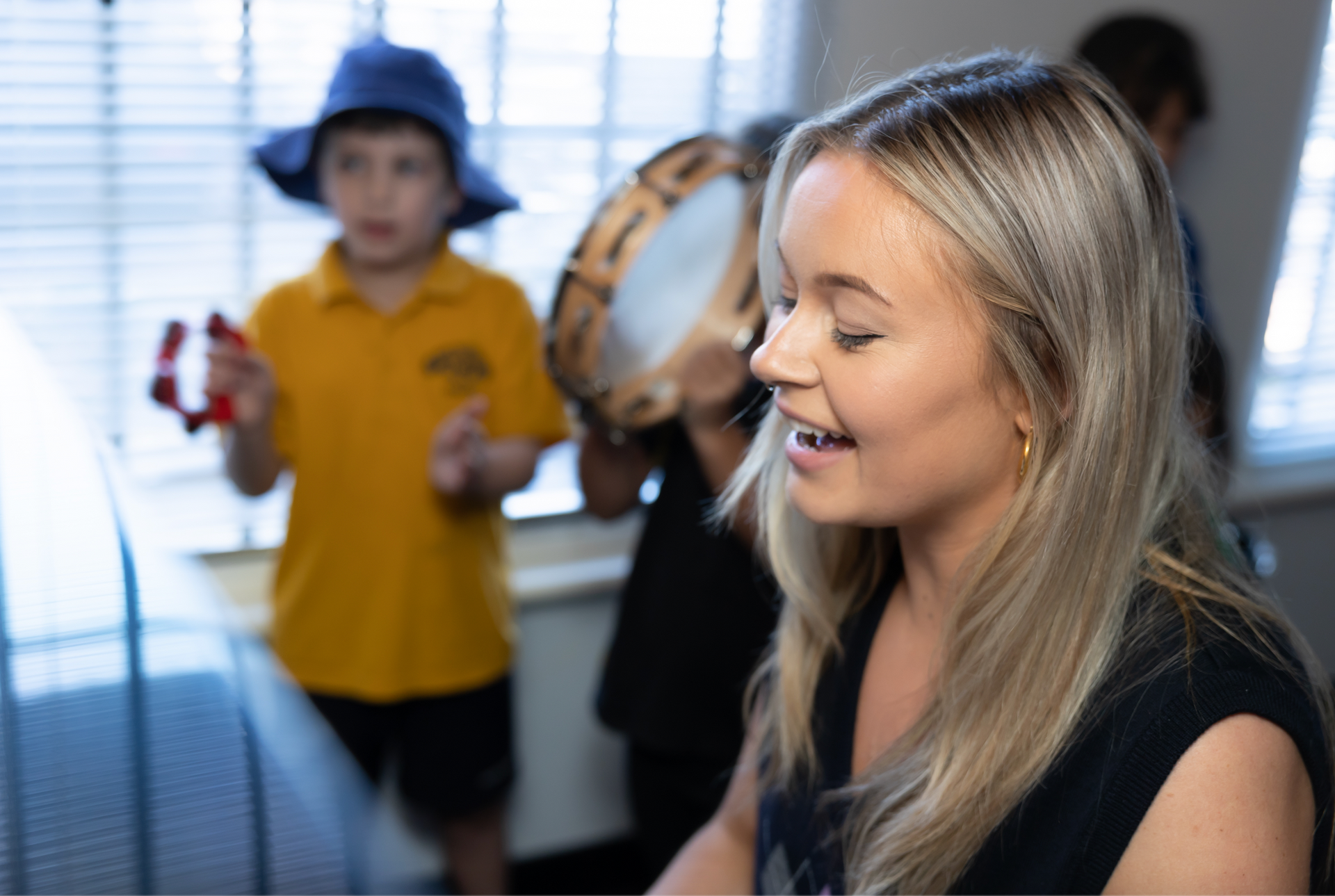 A woman is sitting in front of a group of children playing tambourine.