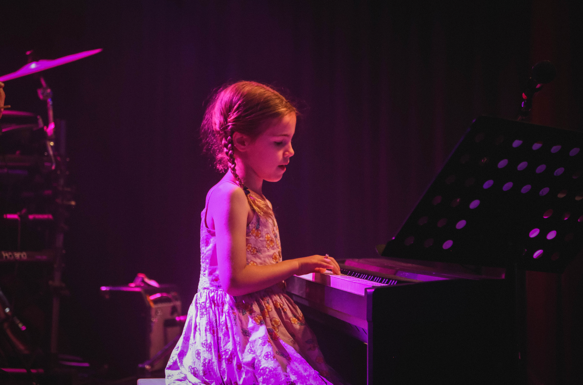 A little girl in a dress is playing a piano on a stage.