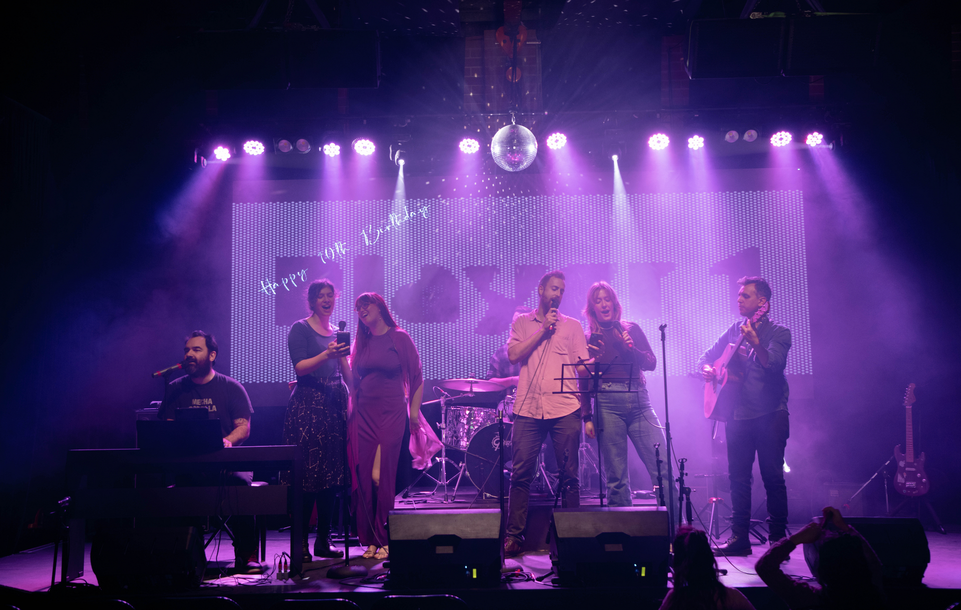 A group of people are standing on a stage with purple lights.