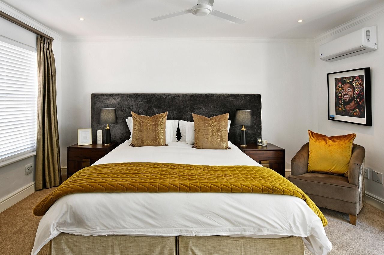 A bedroom with a large bed, gold accents, side tables with lamps, a chair, and a window.