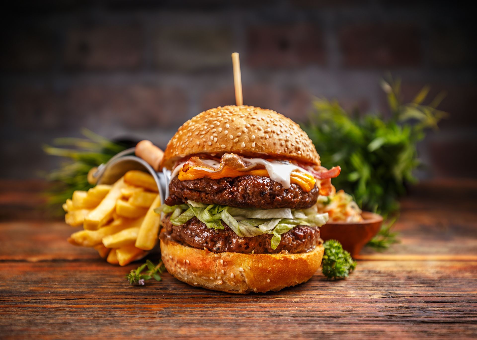 Double-decker burger with fries and greens on a wooden table.