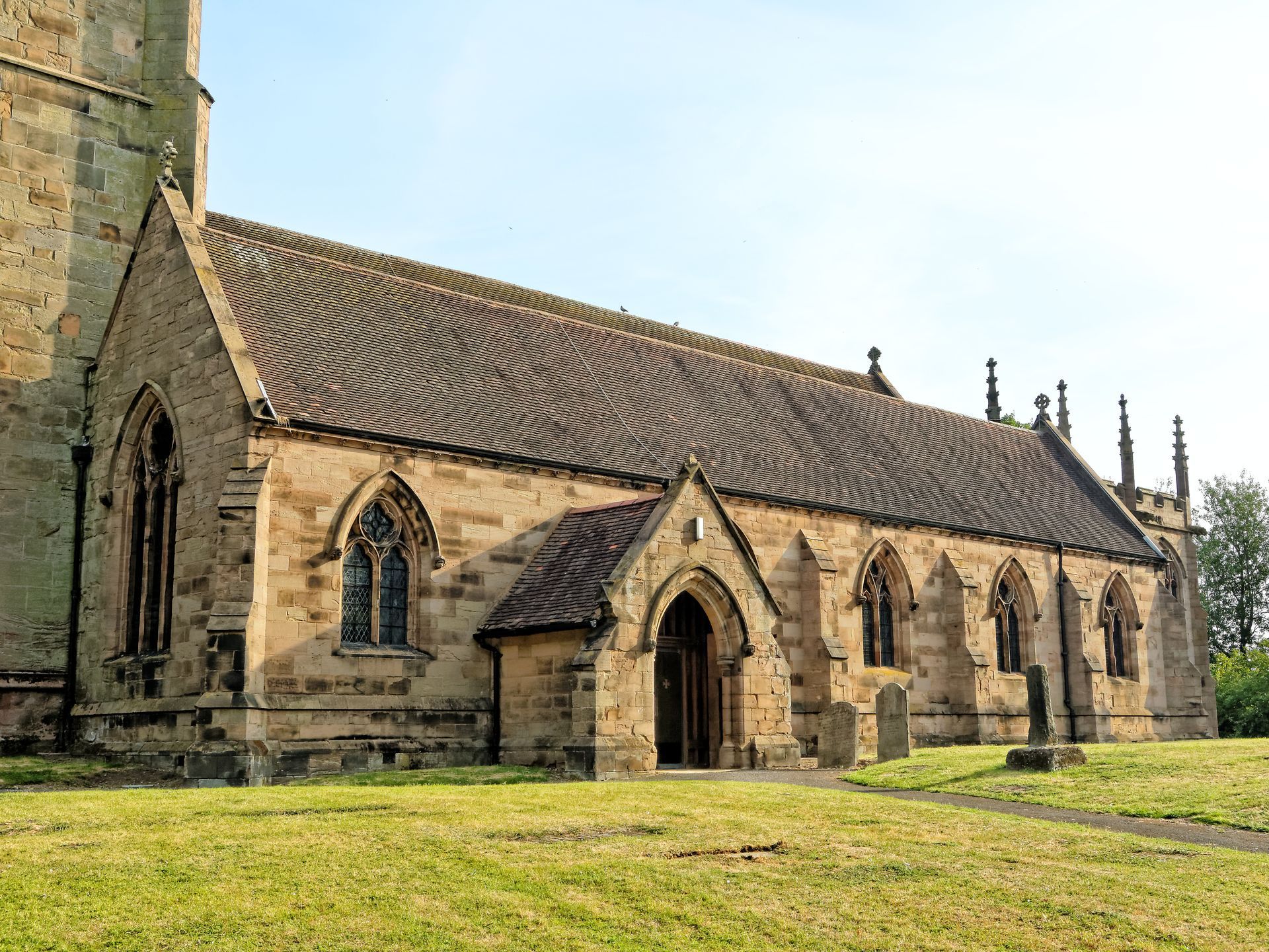 Stone church with arched windows and a tiled roof, in a grassy field.