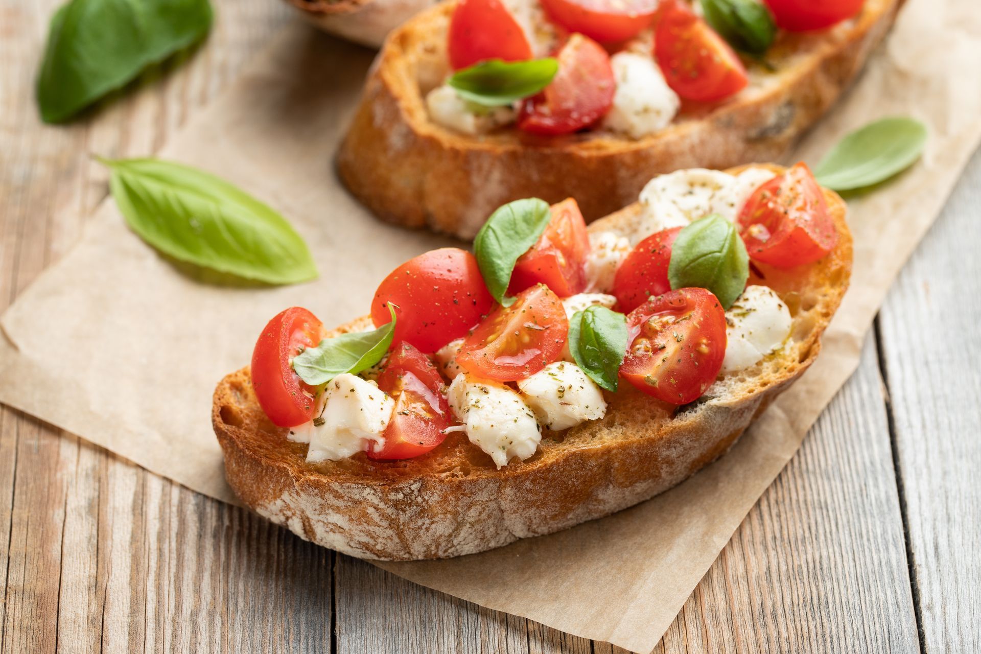Bruschetta with tomatoes, mozzarella, and basil on toasted bread, set on parchment paper.