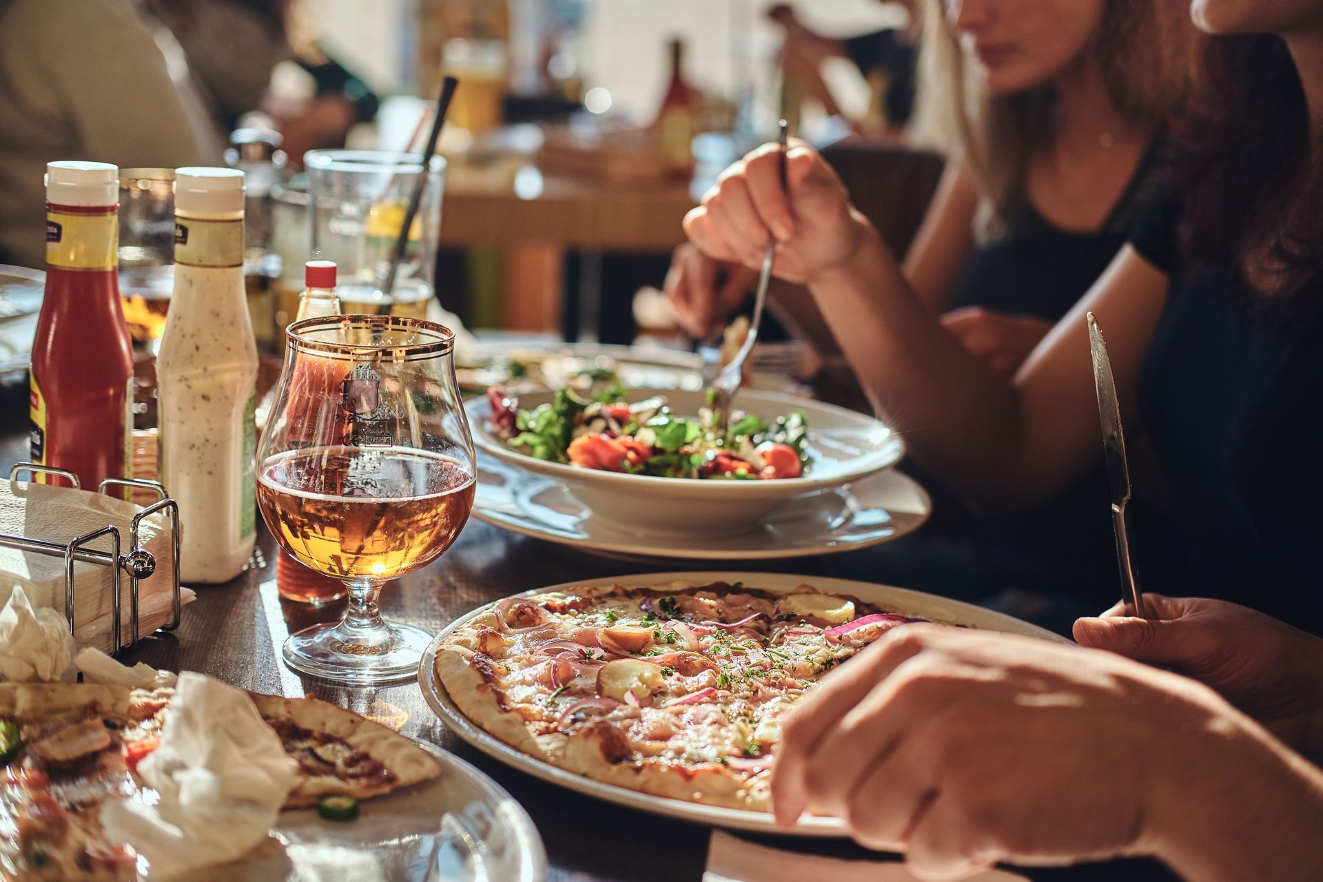 People eating pizza and salad at a restaurant table with drinks.