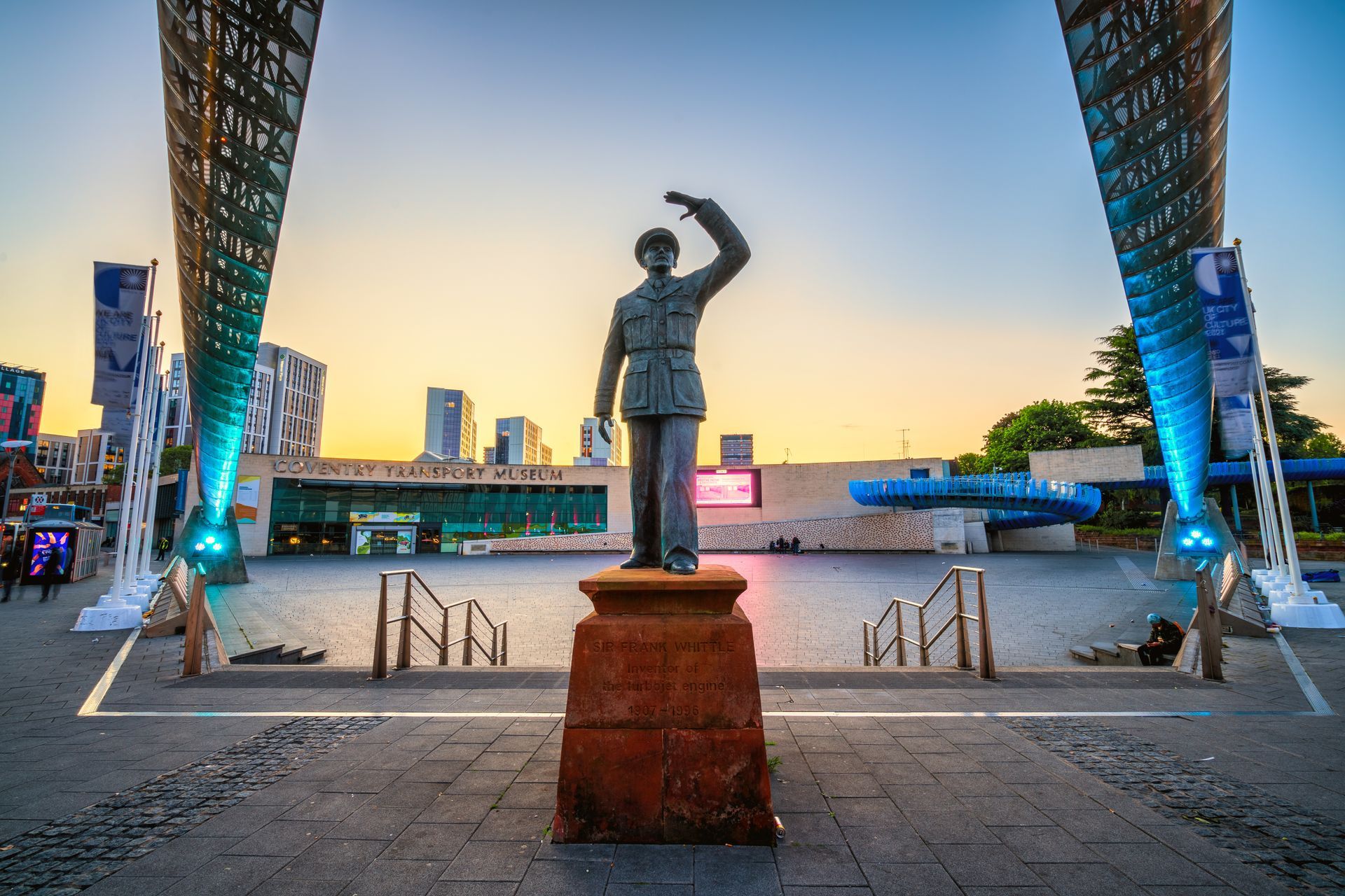 Statue of a man raising a paper above his head in front of a modern building at sunset.