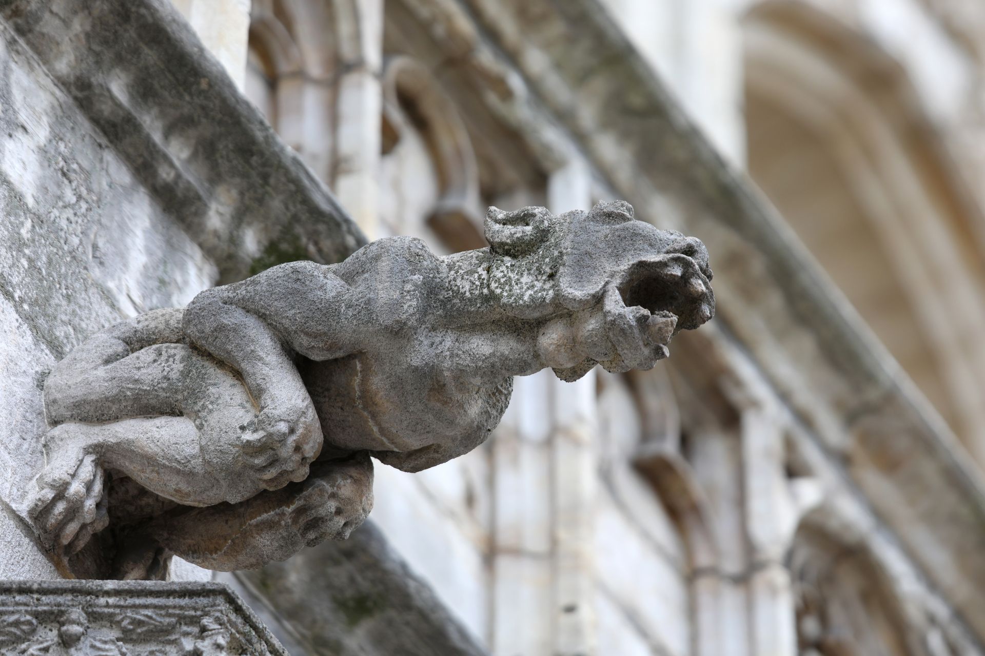 Gargoyle sculpture on a building's facade; stone, monstrous creature with open mouth, detail shot.