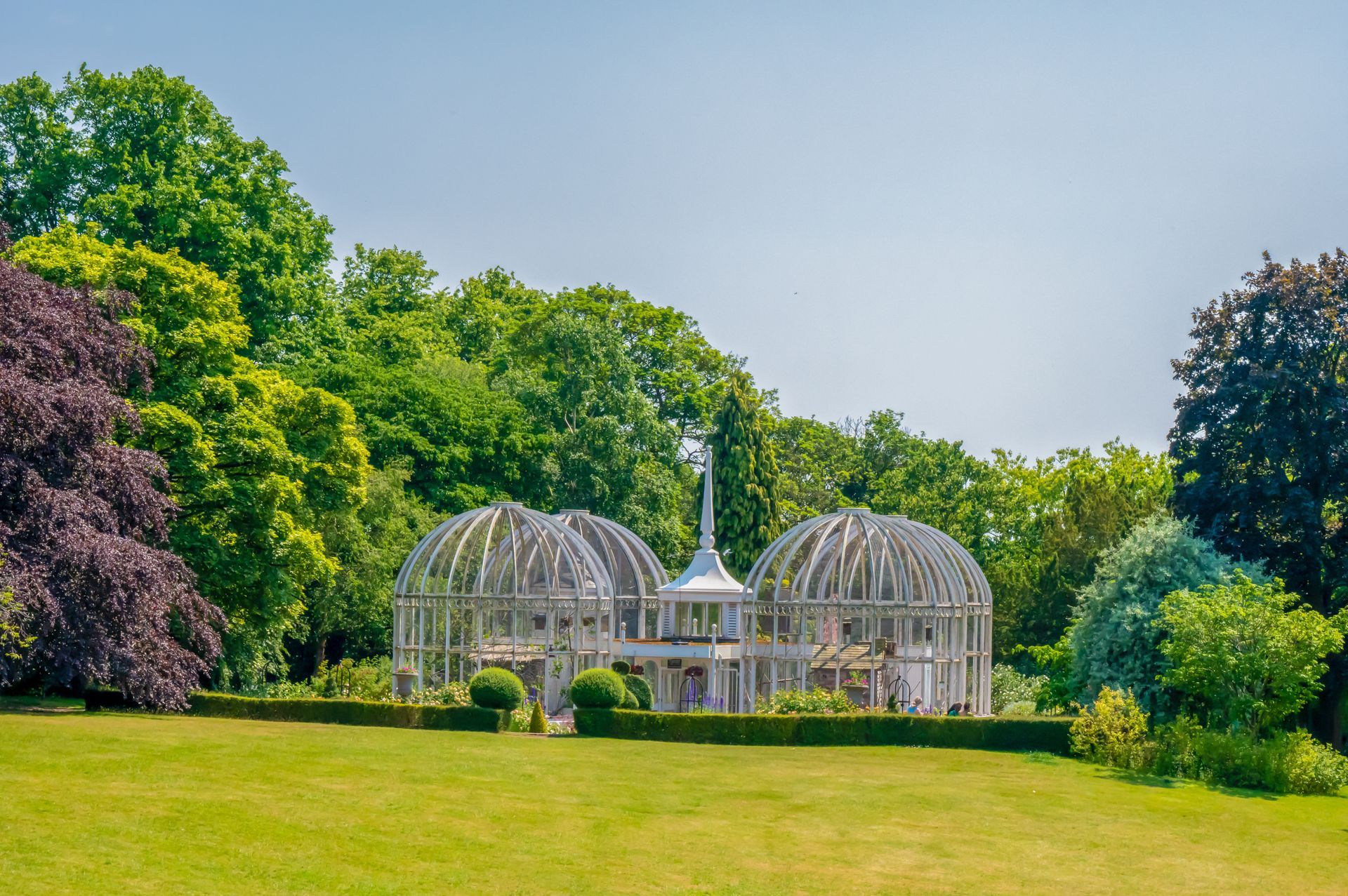 Ornate, white greenhouse domes with central spire, in a lush green garden under a blue sky.