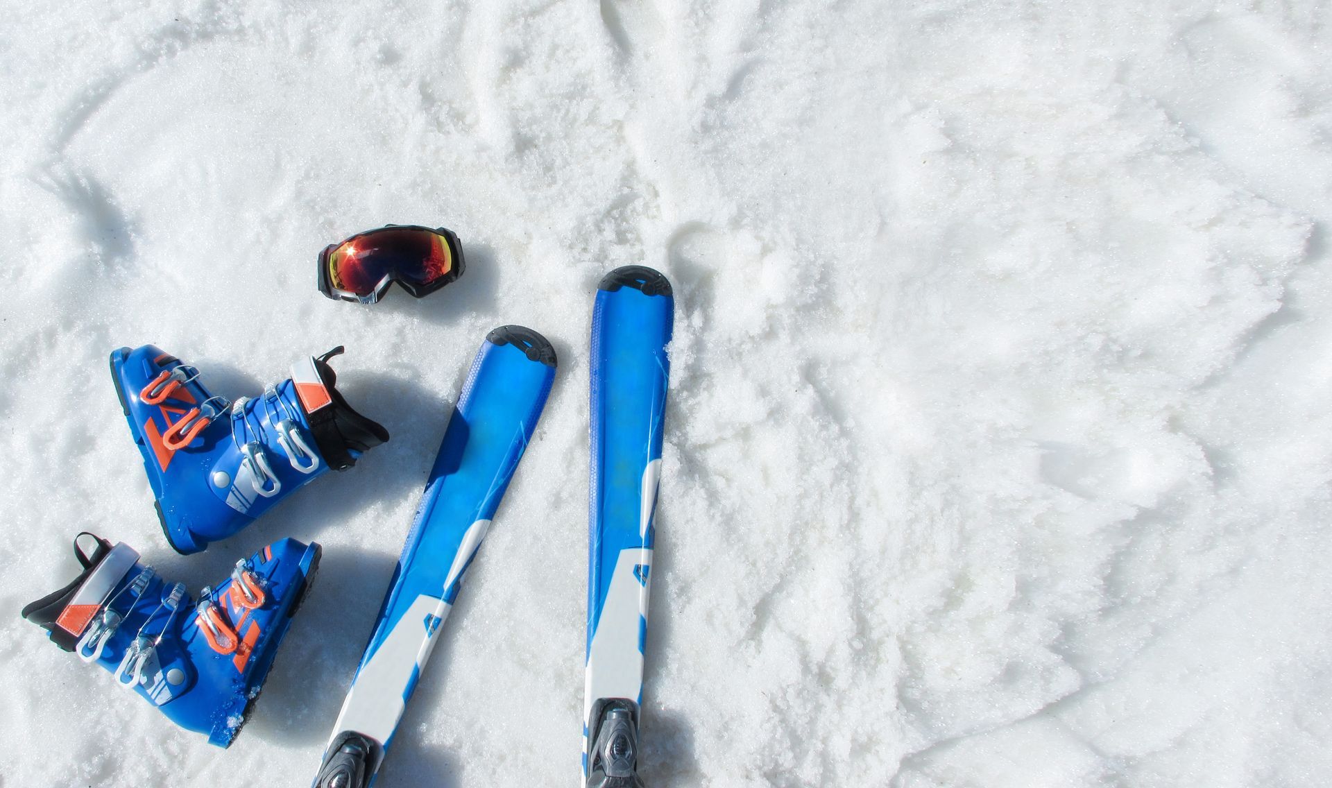 Blue skis, boots, and goggles on a snowy surface.