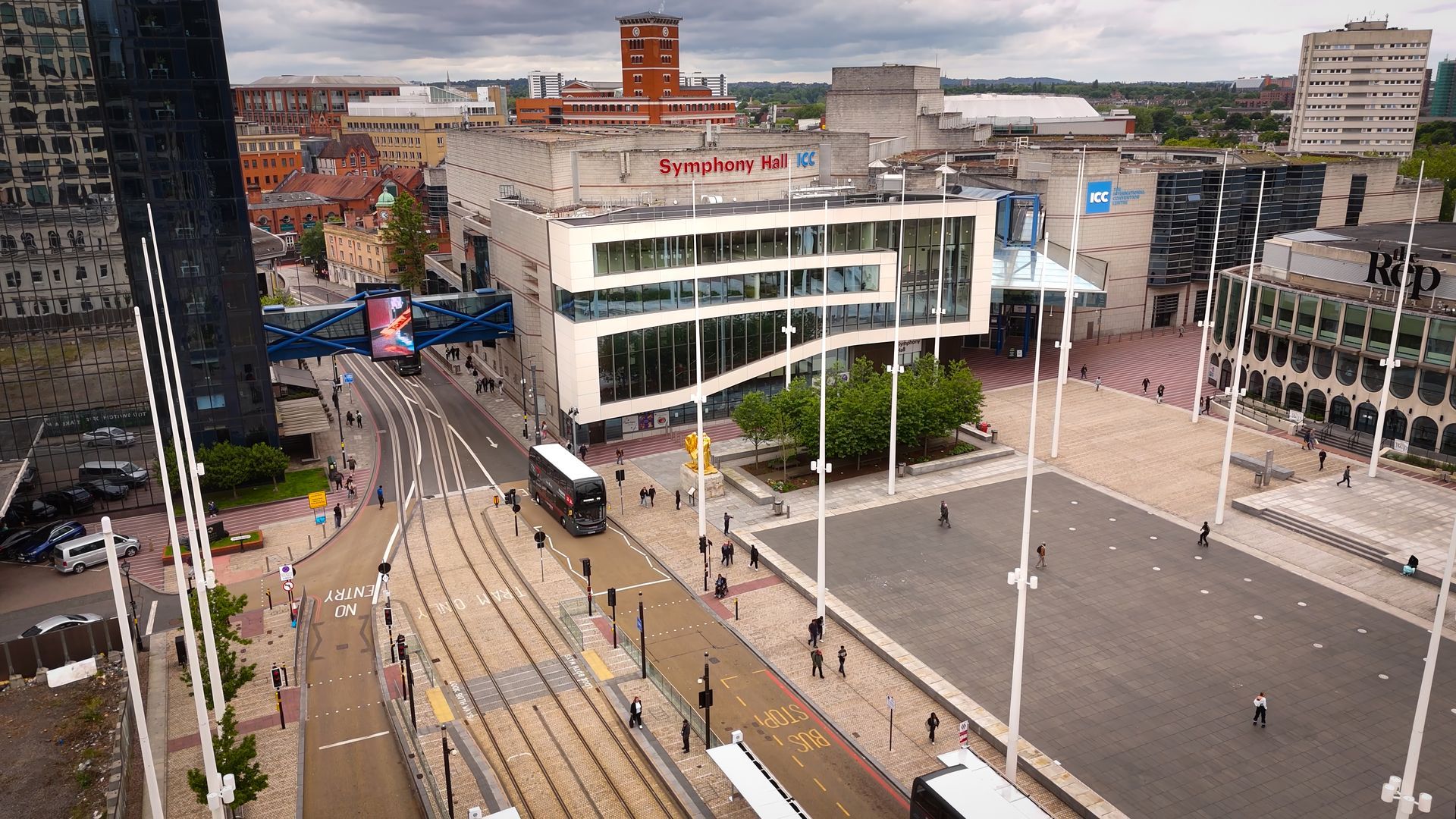 An aerial view of a city square with buildings, a tram, and white flagpoles.