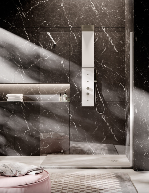 Una moderna cabina doccia con pareti in marmo scuro, pannello doccia bianco e mensola incassata, illuminata dalla luce naturale del mattino.