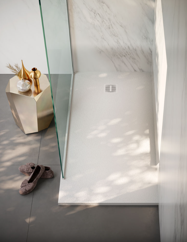 Un piatto doccia in stile marmo bianco con parete divisoria in vetro, un tavolino laterale dorato e mocassini su un pavimento piastrellato grigio.