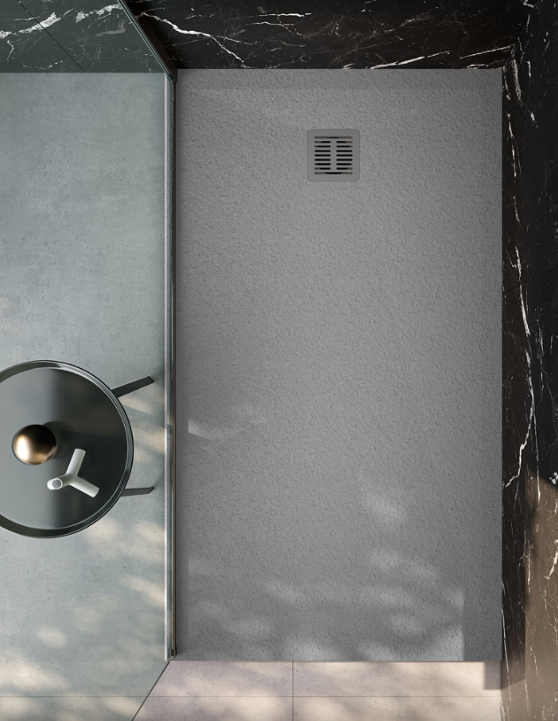 Vista dall'alto di un piatto doccia rettangolare grigio con scarico centrale quadrato, incastonato in uno sfondo di marmo scuro e pavimento in cemento.