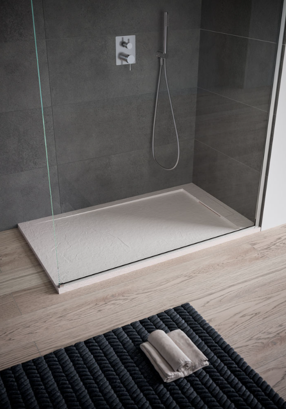 Una moderna cabina doccia con base grigio chiaro, pareti rivestite con piastrelle scure, doccetta a mano e un asciugamano piegato sul pavimento.