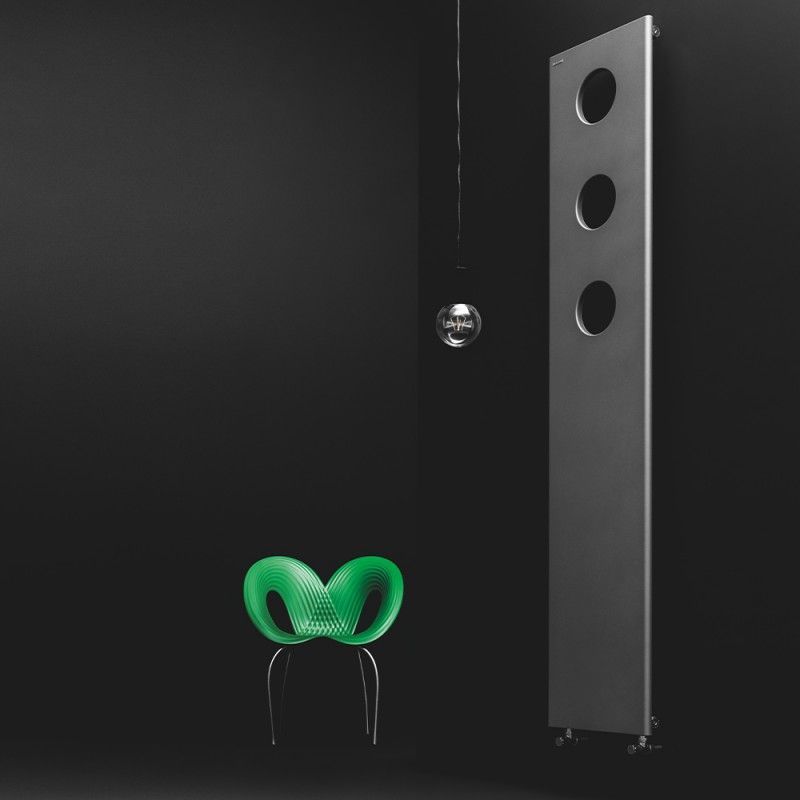 In una stanza buia, accanto a un alto termosifone grigio verticale con tre aperture circolari, si erge una sedia scultorea di un verde brillante.