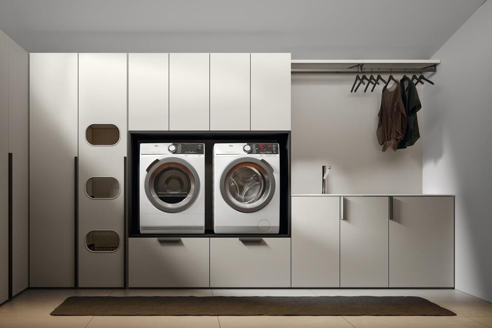 Una lavanderia moderna e dai colori chiari, con lavatrice e asciugatrice integrate, armadietti e uno stendino per i vestiti.