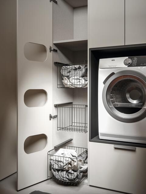 Un moderno mobile lavanderia con cestelli estraibili in filo metallico per la biancheria, posizionato accanto a un'asciugatrice integrata, in una stanza elegante dai toni neutri.