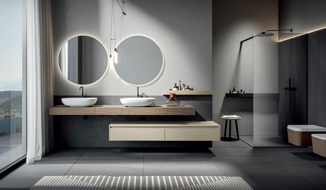 Bagno moderno e minimalista con doppio lavabo, due specchi rotondi retroilluminati, piano d'appoggio sospeso e cabina doccia.