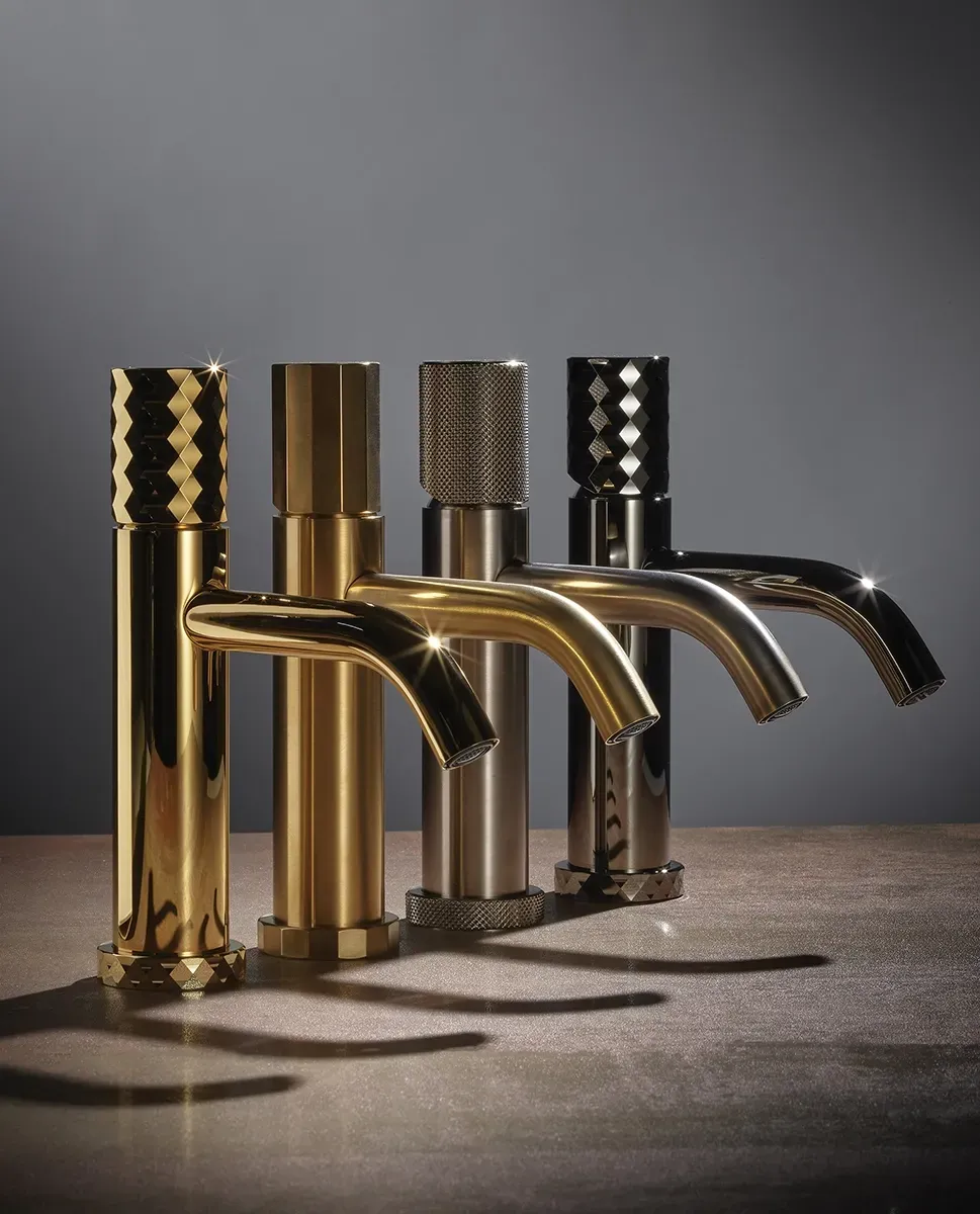 Quattro rubinetti da bagno di lusso con diverse finiture metalliche, allineati su una superficie su uno sfondo grigio scuro.