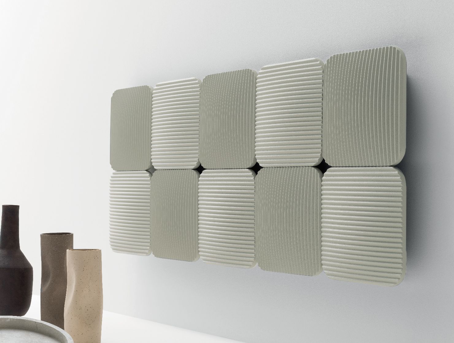 Un radiatore a parete composto da dieci pannelli quadrati grigio chiaro con diverse fantasie geometriche a linee e texture.