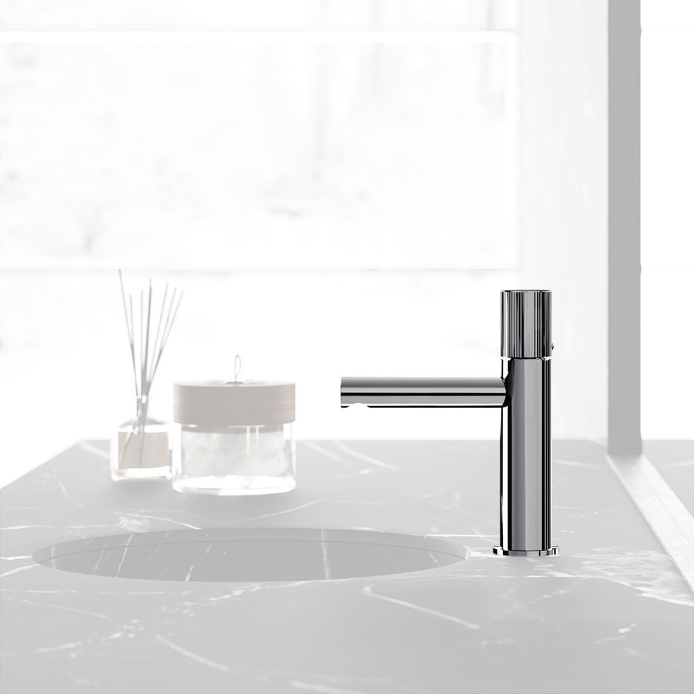 Un elegante rubinetto da bagno con finitura cromata, posizionato al centro di un piano in marmo bianco accanto a un diffusore a bastoncini di vetro.