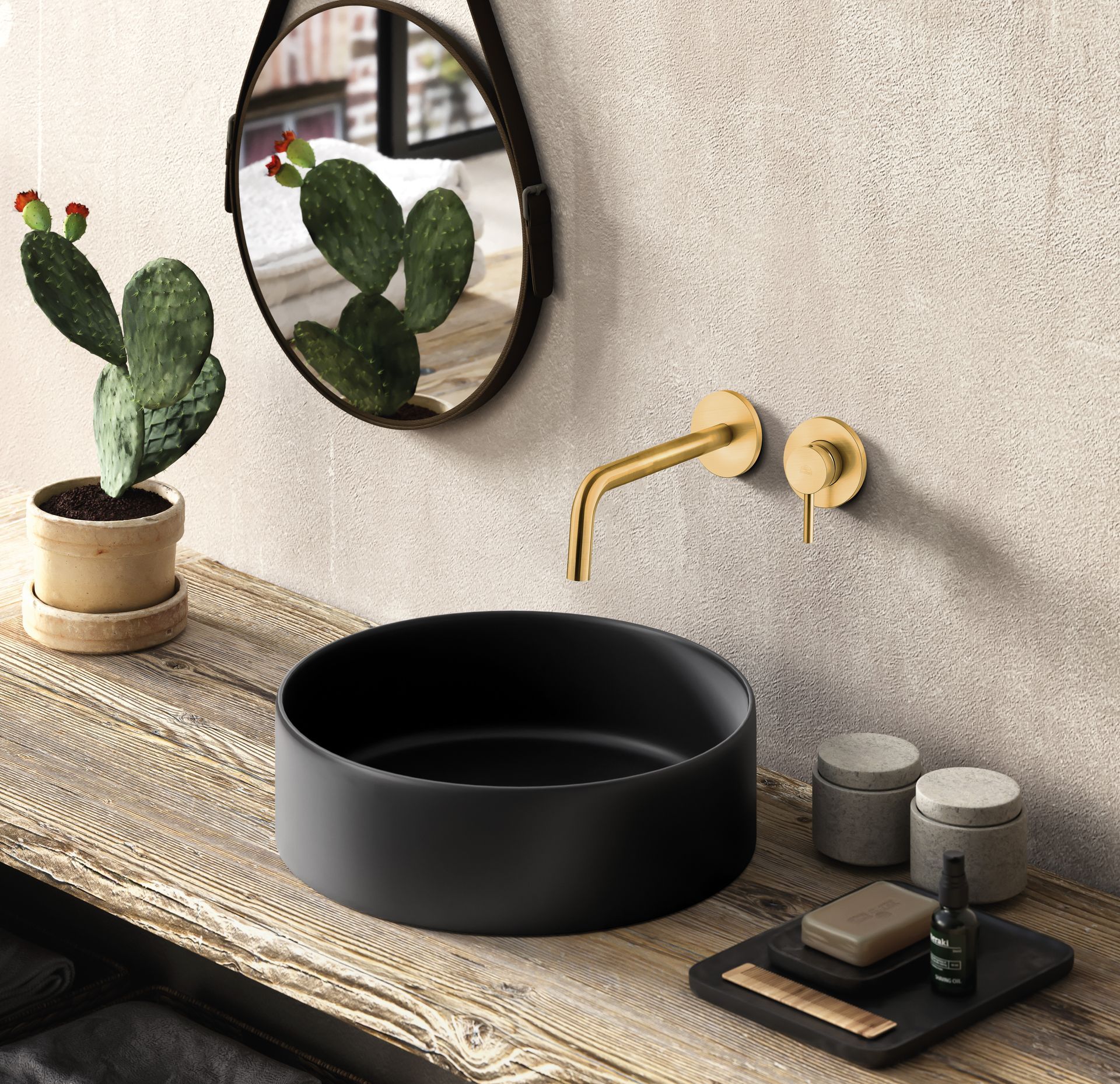 Un mobile bagno moderno con lavabo a ciotola nero opaco, rubinetto a parete dorato, specchio rotondo e un piccolo cactus.