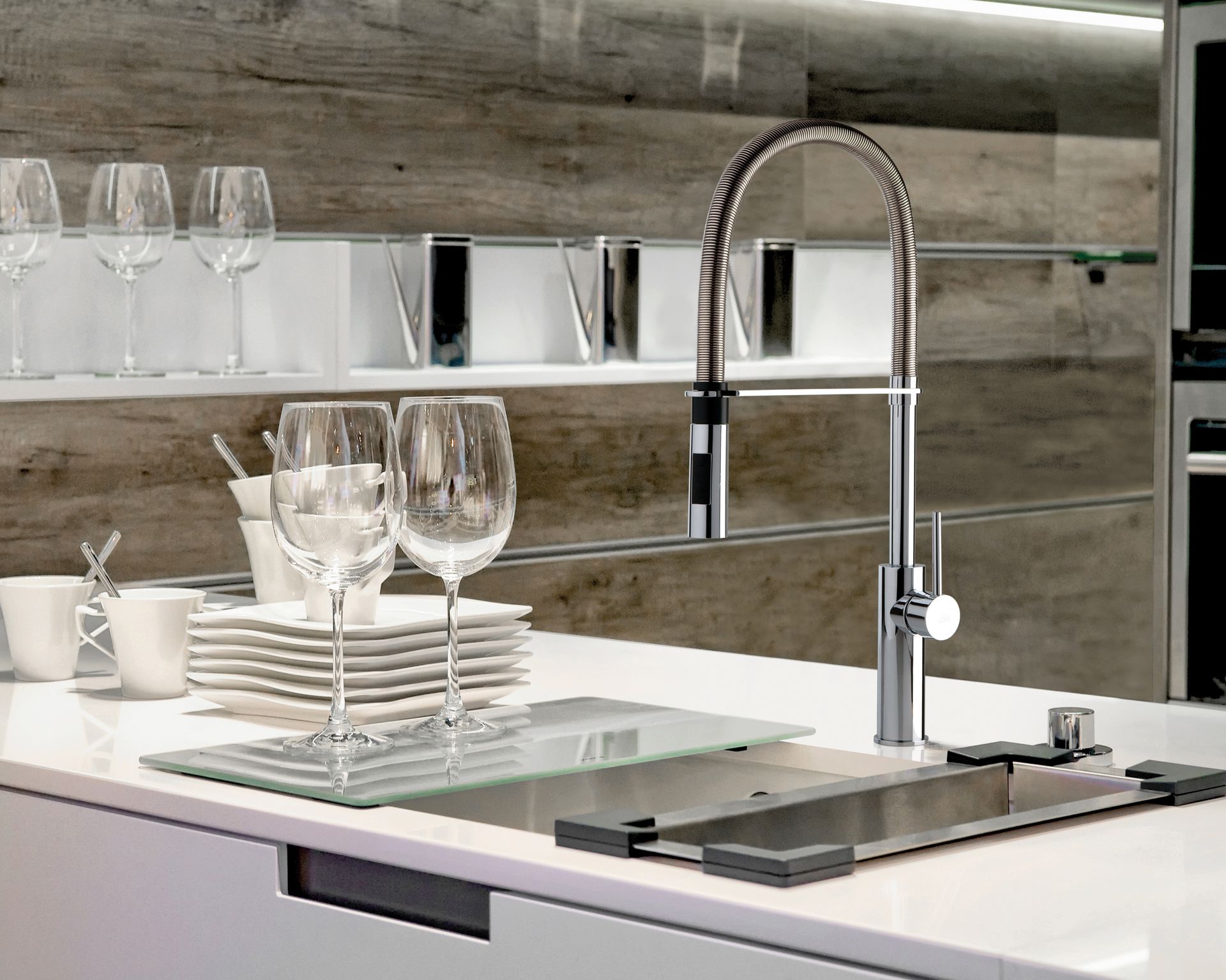 Un'isola cucina moderna con rubinetto cromato, piatti bianchi impilati, bicchieri da vino e paraschizzi in legno.