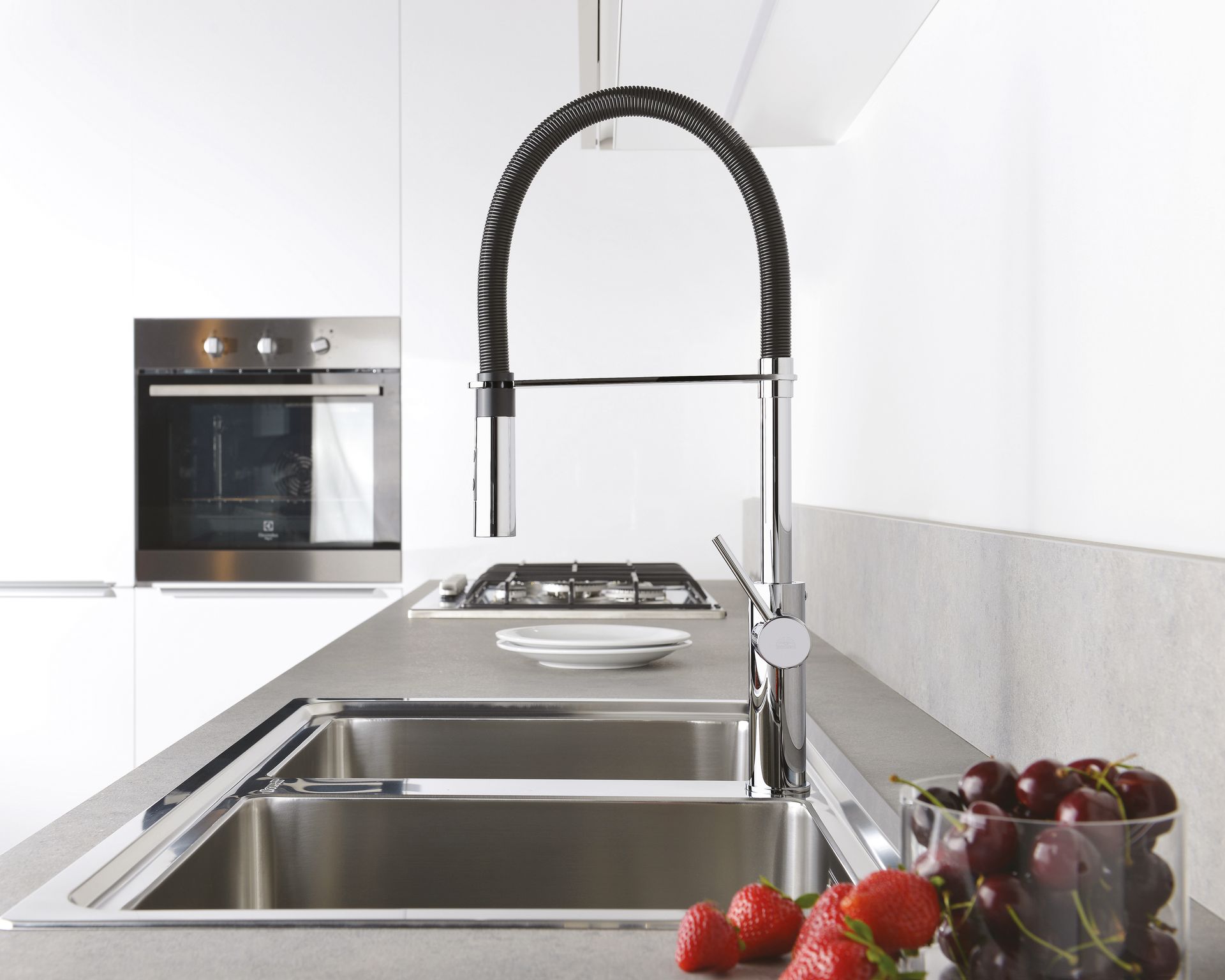 Cucina moderna con rubinetto a spirale nero ad arco alto sopra un doppio lavello in acciaio inox, con frutta in primo piano.
