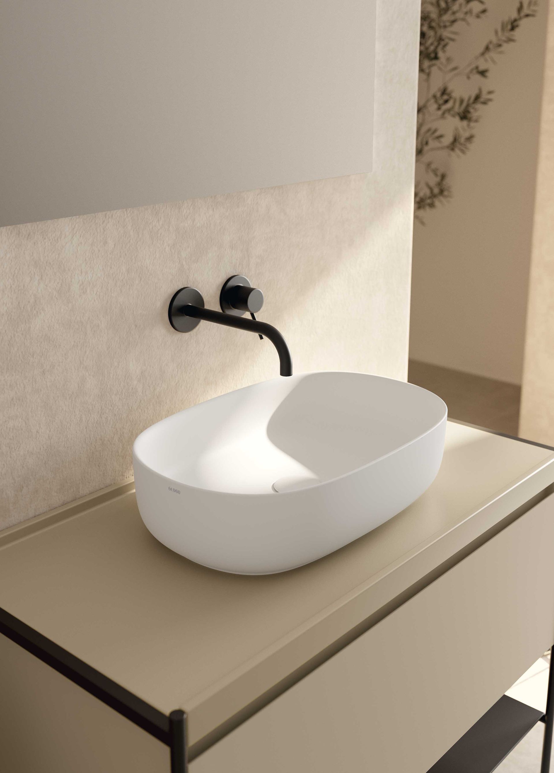 In un bagno moderno, un lavabo ovale bianco con rubinetto a parete nero opaco, posizionato su un mobiletto beige.