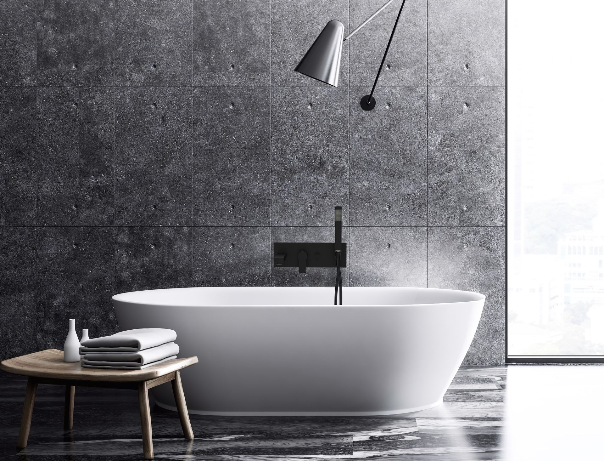 Una moderna vasca da bagno freestanding di colore bianco è posizionata di fronte a una parete rivestita di piastrelle scure e texturizzate, con uno sgabello e degli asciugamani in primo piano.