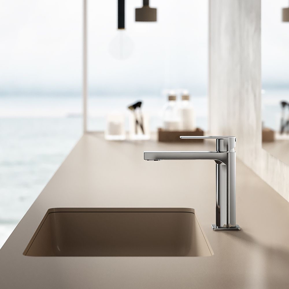 Mobile bagno moderno con rubinetto in cromo lucido e lavabo integrato beige, su uno sfondo sfocato che richiama una costa.