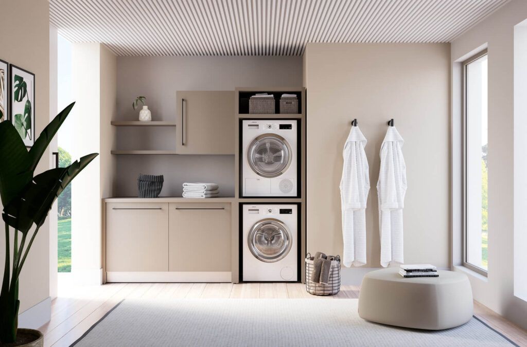 Una moderna zona lavanderia con lavatrice e asciugatrice sovrapposte, armadietti adiacenti, appendiabiti a muro con accappatoi e pouf a pavimento.