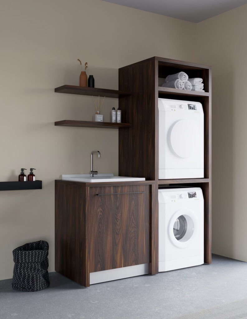 Una lavanderia moderna con mobili in legno scuro, lavabo, mensole a muro, lavatrice e asciugatrice impilabili e un cestino per la spazzatura.