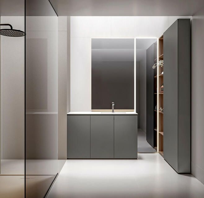 Un bagno moderno e minimalista caratterizzato da un mobile lavabo grigio con specchio, una cabina doccia e mensole a vista su pareti bianche.