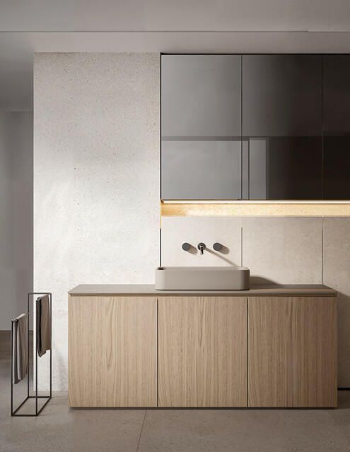 Mobile bagno minimalista con mobiletto in legno chiaro, lavabo a bacinella grigio, rubinetto a parete e pensili scuri.