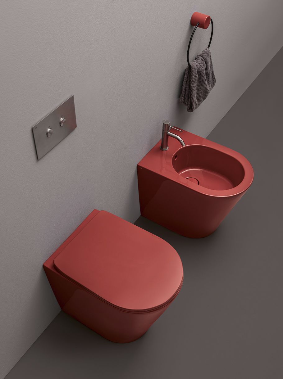 Un moderno set composto da WC e bidet sospesi, di colore rosso intenso, con anello portasciugamani rosso abbinato e asciugamano grigio, su una parete chiara.