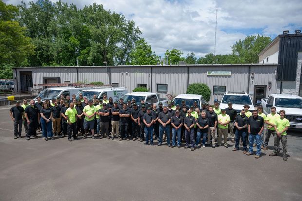 Large group of people in black and yellow shirts, posing in front of several vans and a building. Large group of people in black and yellow shirts, posing in front of several vans and a building.