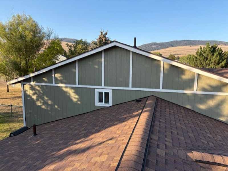 An elevated view of a green house exterior with vertical wood siding, white trim, and a shingled roof under a clear sky.