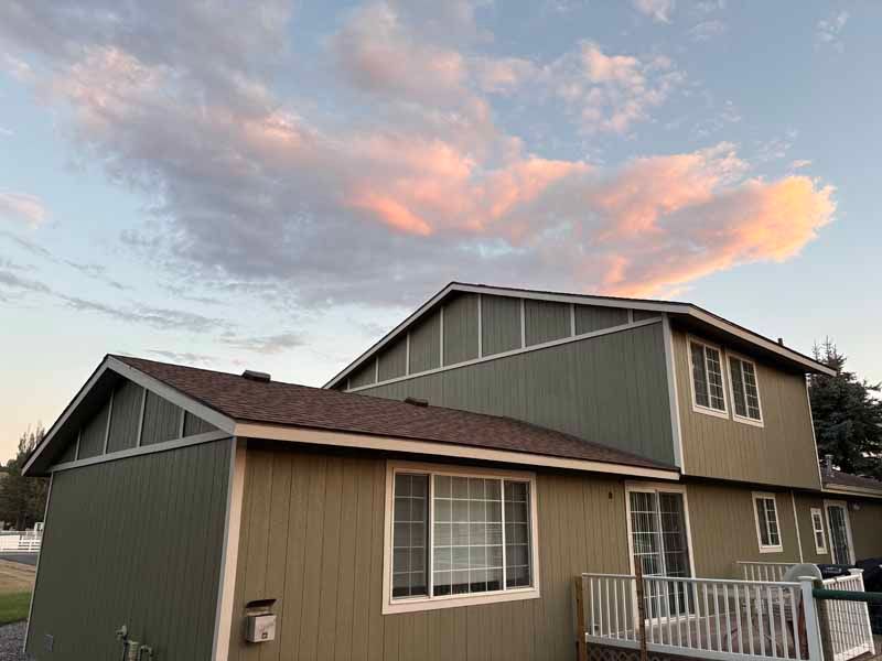 A tan two-story house with green vertical siding under a sky with pink-tinted clouds at sunset.
