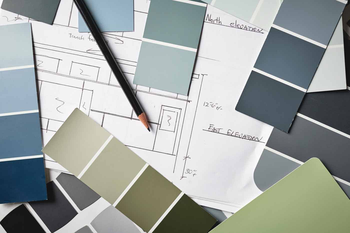 Paint swatches in shades of blue, gray, and green are spread over an architectural floor plan with a pencil.
