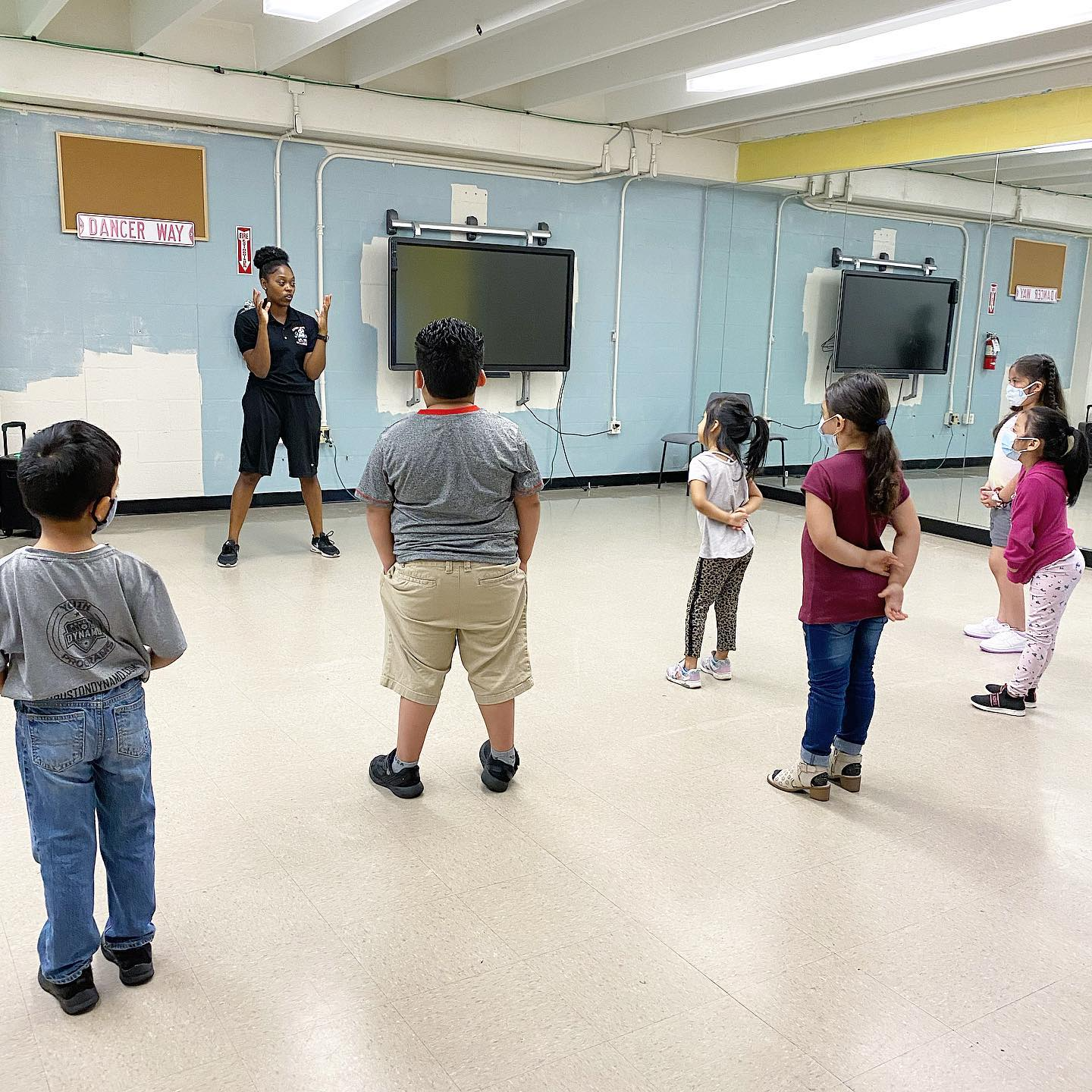 A group of children are standing in a room with a man standing in front of them