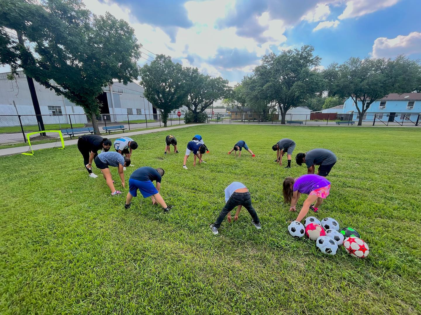 A group of people are doing stretching exercises in a park with soccer balls.