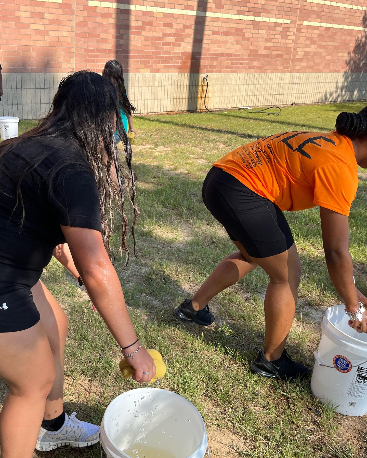 Two women are washing their hair in buckets in a park.