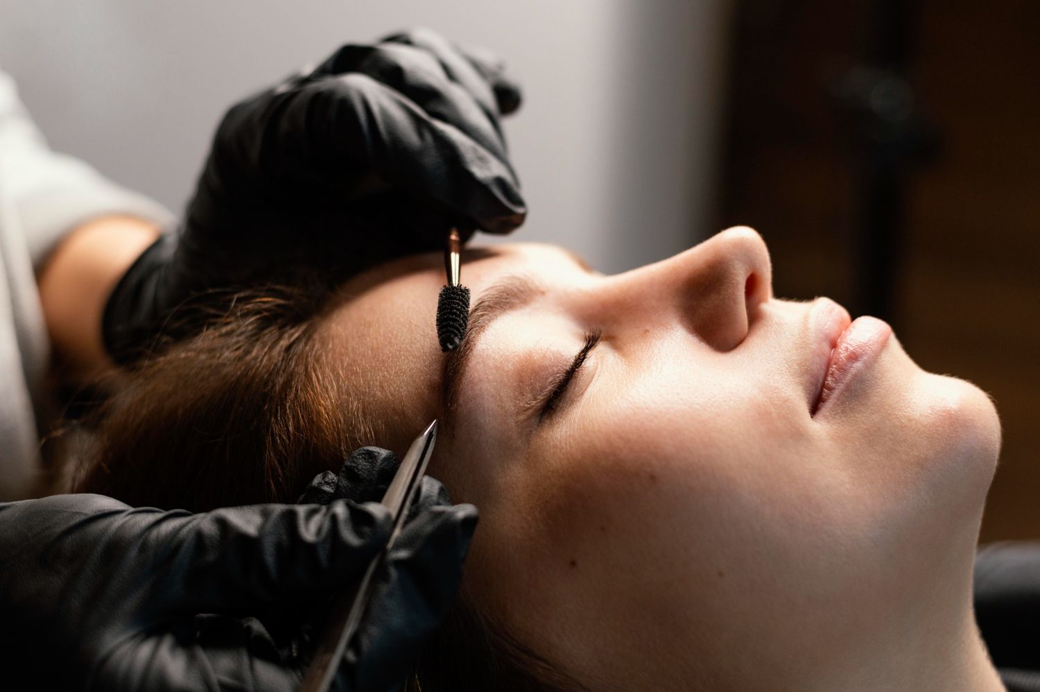 A woman is getting her eyebrows tattooed by a tattoo artist.