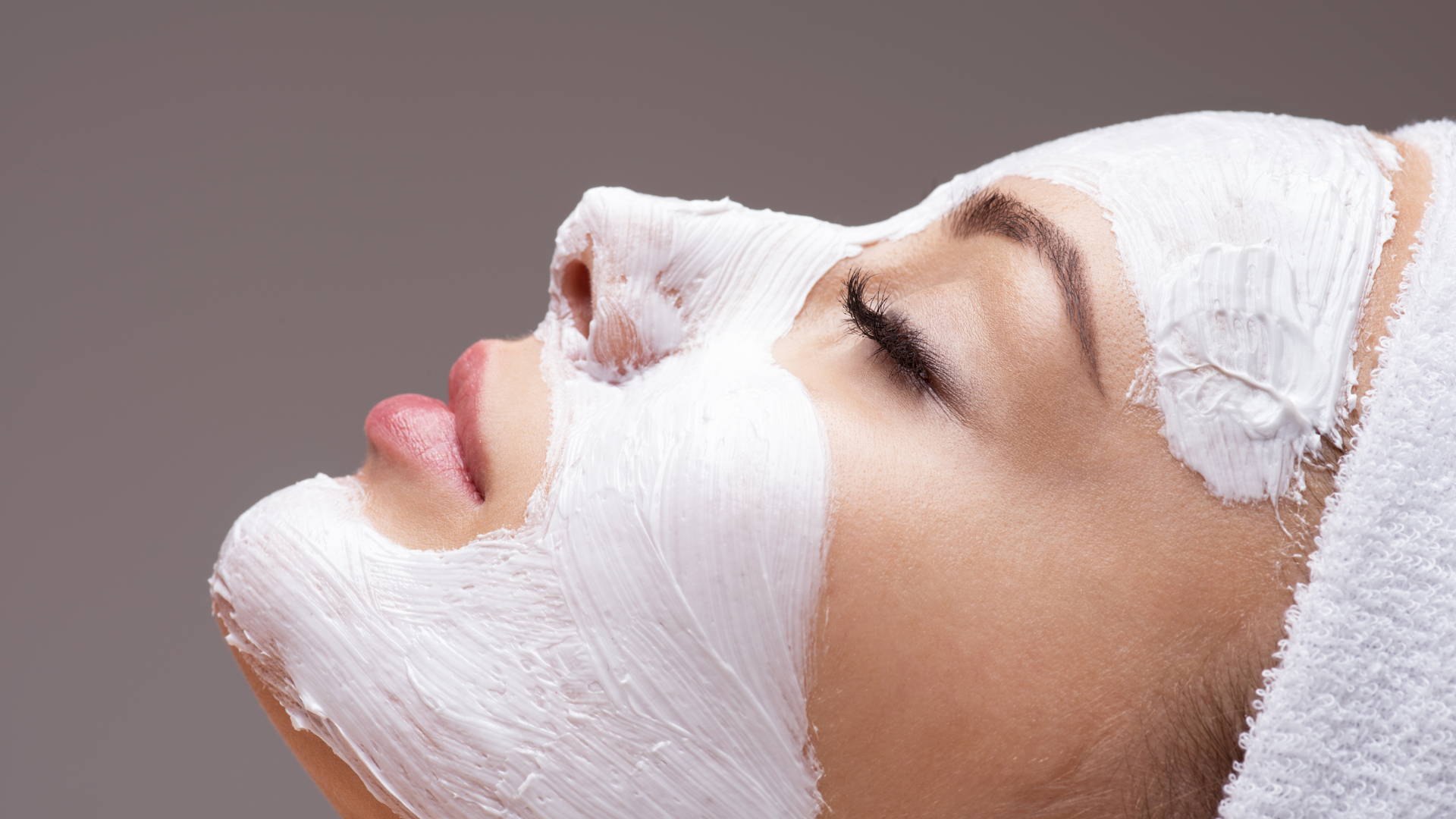 A woman is getting a facial treatment with a white mask on her face.