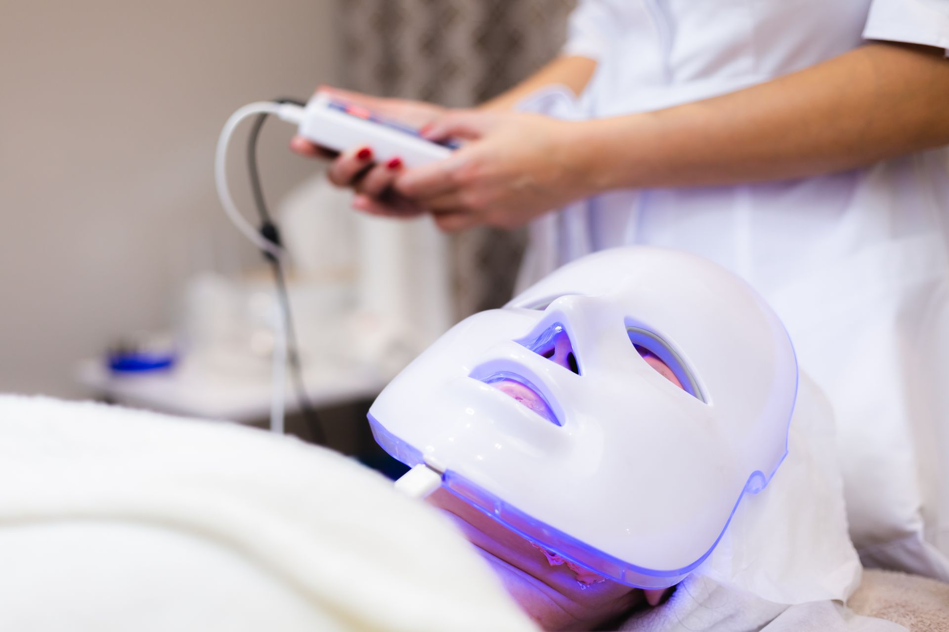 A woman is getting a facial treatment with a light mask on her face.