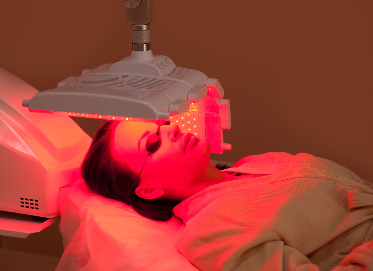 A woman is laying on a bed with a red light on her face.